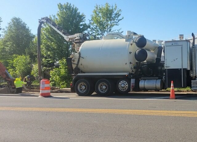ABI hydrovac working a live roadway with the boom deployed, cones set and a crew member in hi-vis